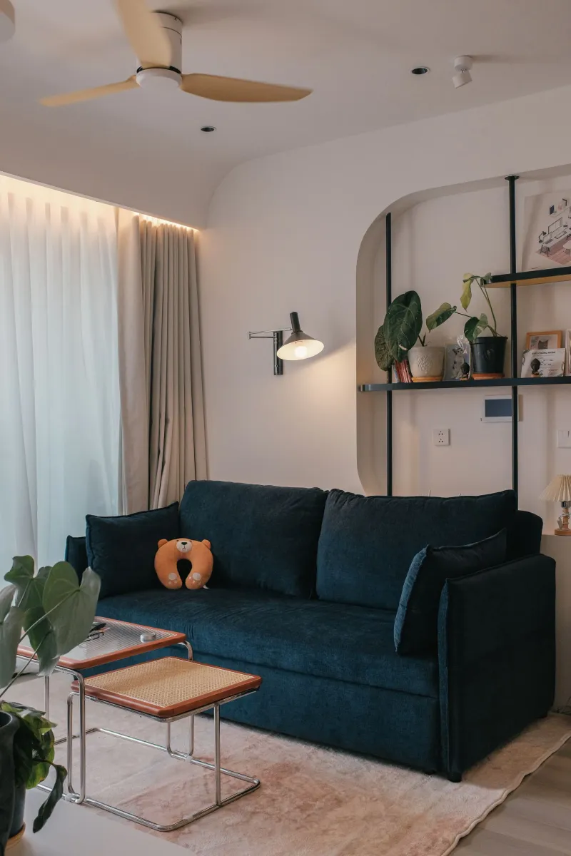 Sala com sofá azul-marinho, estante de ferro e plantas